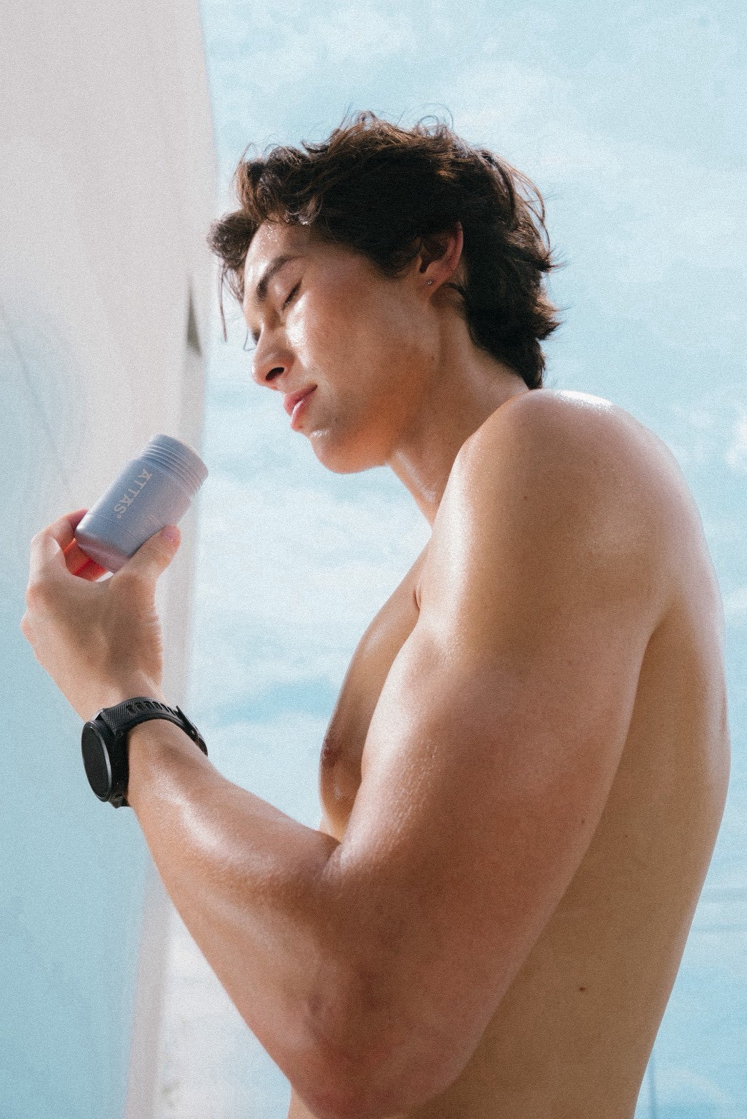 Man applying ATTAS deodorant stick against a blue sky